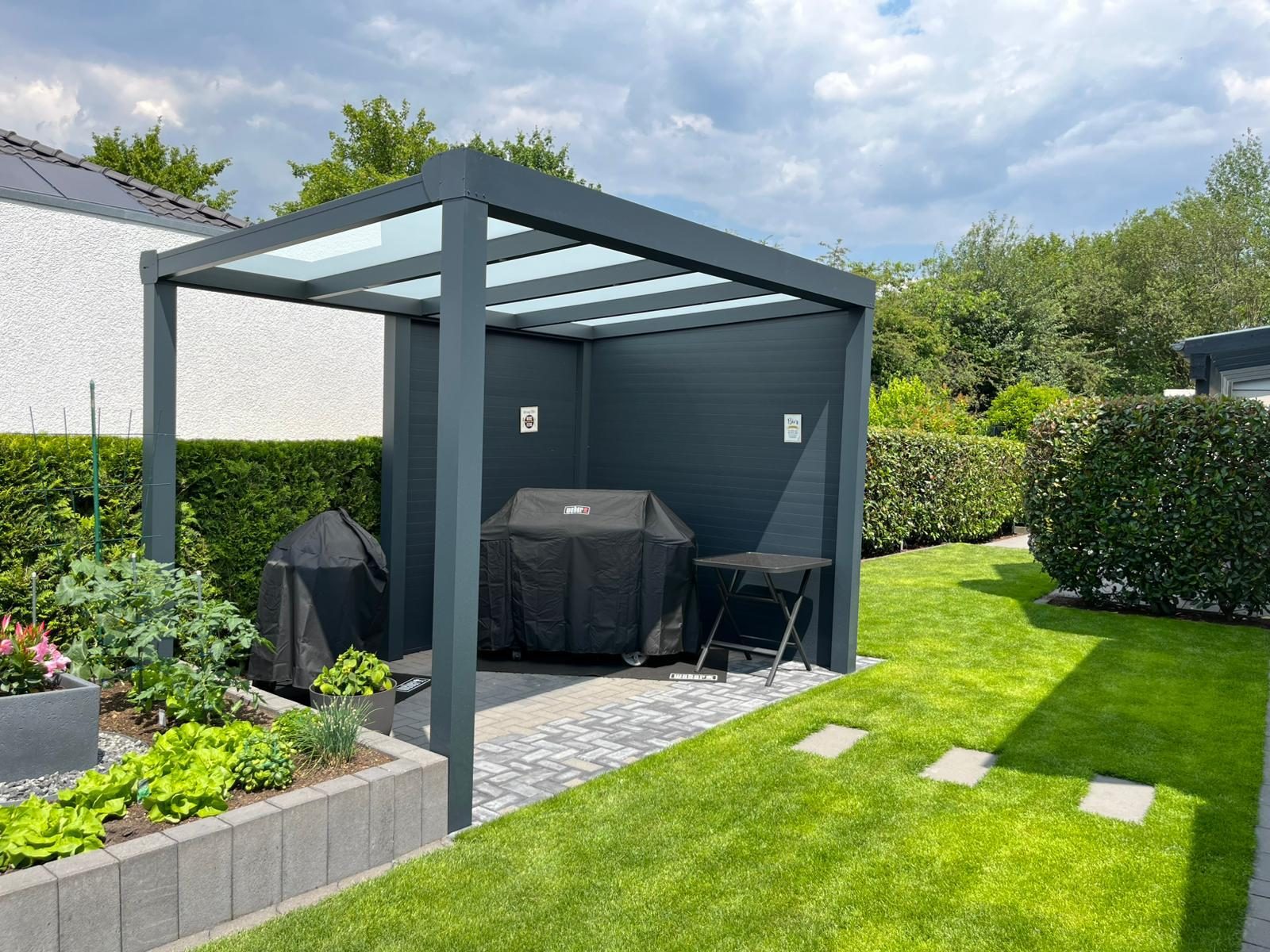 Freistehende Aluminium-Pergola mit festem Dach und Seitenwand in einem Garten in NRW